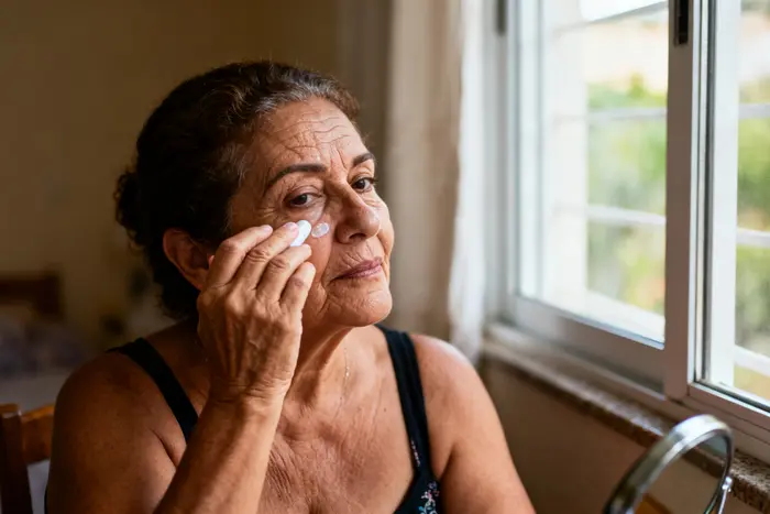 Mulher de 55 anos aplicando protetor solar ao redor dos olhos, rotina diária para cuidar da pele com colágeno Verisol