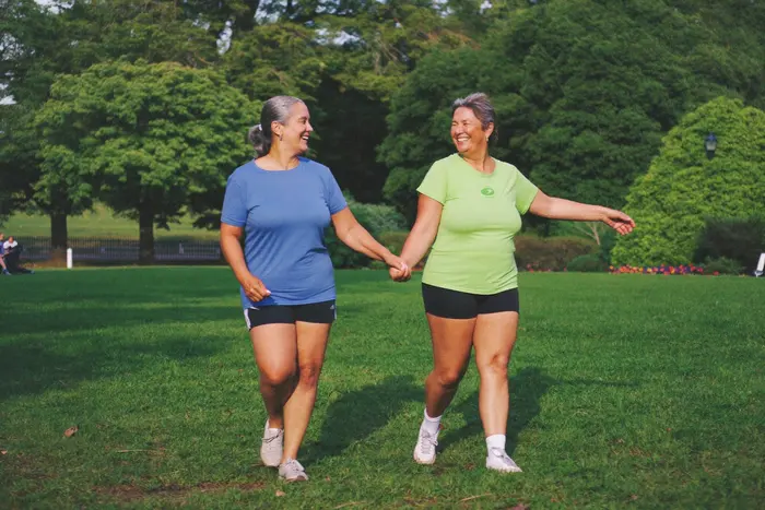 Duas amigas de mais de 50 anos caminhando e rindo num parque