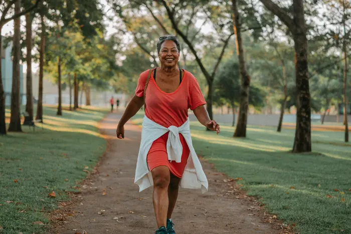 Mulher de uns 55 anos caminhando sorridente num parque arborizado